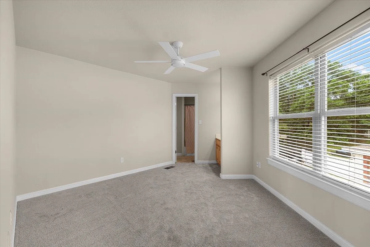 Carpeted room featuring a ceiling fan, a large window with blinds, and light-toned wall paint