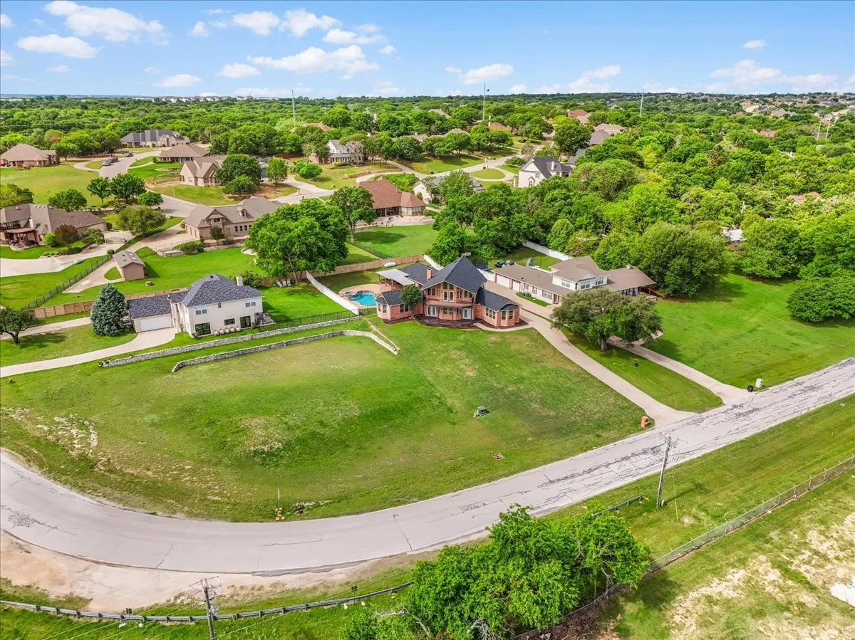 Expansive residential lot featuring a manicured lawn, established landscaping, and a curvilinear paved road frontage