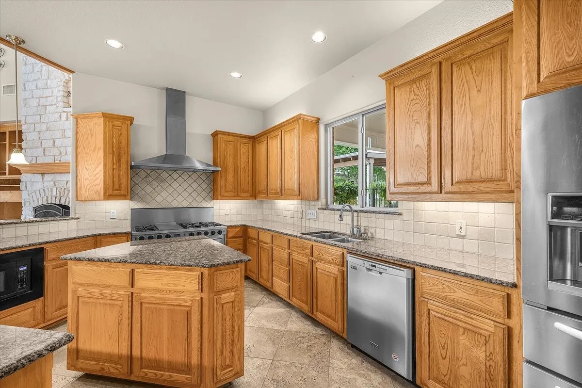 Gourmet kitchen with wood cabinetry, granite countertops, tile flooring, and stainless steel appliances including a double oven range with a matching range hood