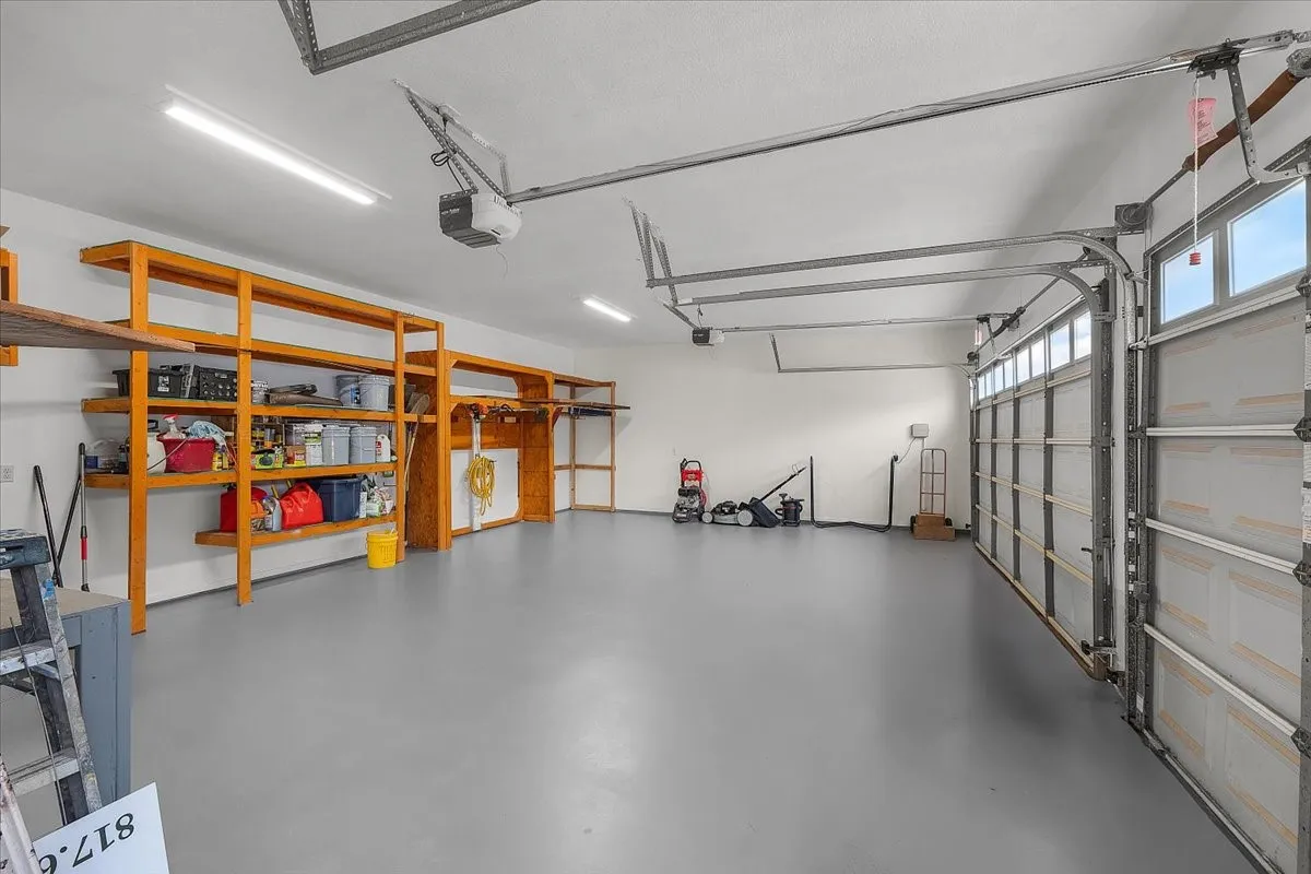 Spacious garage featuring a durable gray floor, built-in wooden shelving, multiple fluorescent lighting fixtures, and a garage door with upper window panels