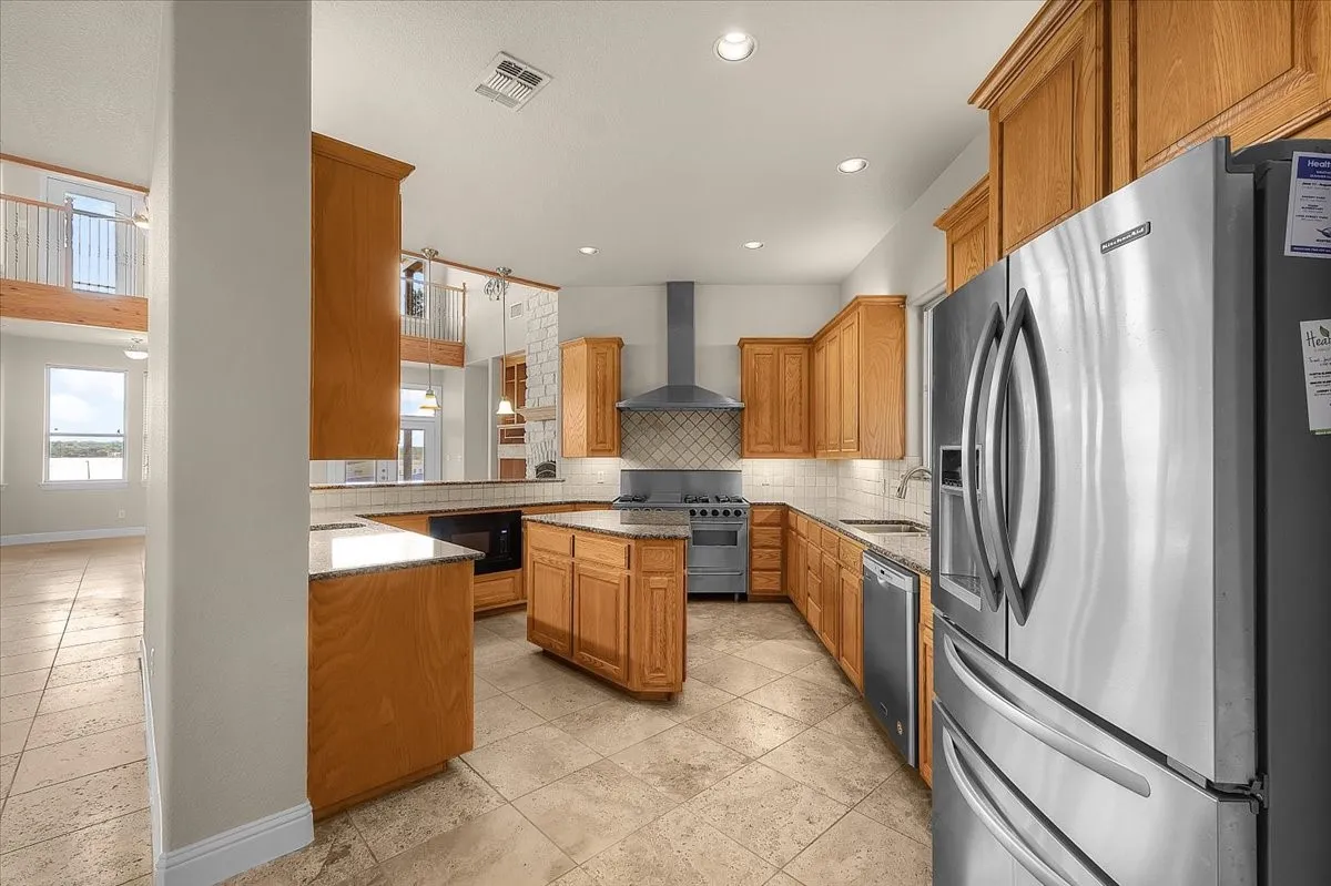 U-shaped kitchen featuring light wood cabinetry, stone-finish countertops, stainless steel appliances, a center island, and tiled flooring
