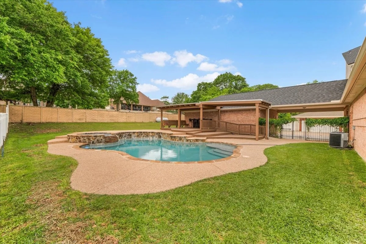 Backyard oasis featuring a curvilinear pool with integrated spa and stone surround