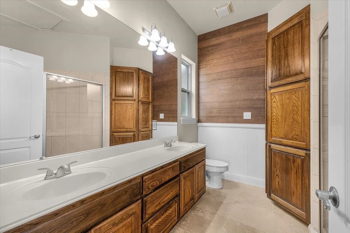 Bathroom featuring a long dual vanity with integrated sinks, wood-finish cabinetry, a framed glass shower enclosure, and a shiplap accent wall