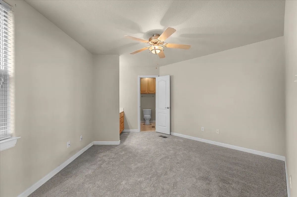 Spacious room featuring neutral-toned walls, gray carpeting, a window with blinds, and a ceiling fan with integrated lighting