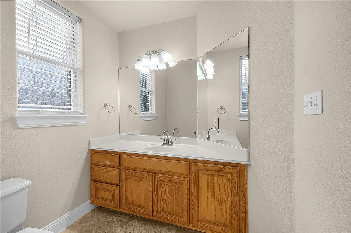 Bathroom vanity featuring a light wood-finish cabinet, dual sinks, a white countertop, and a large wall-mounted mirror