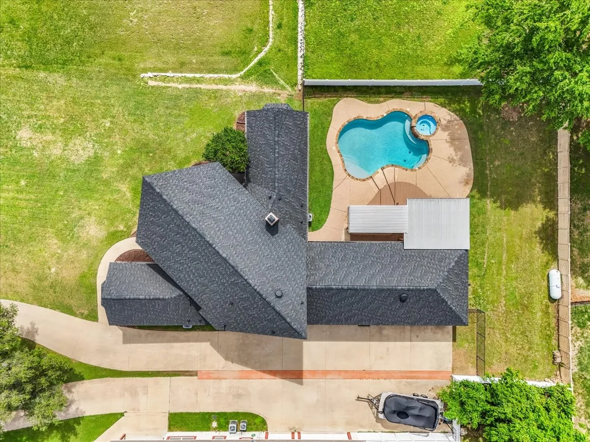 Expansive property featuring a dark shingle roof, a generously sized swimming pool with an integrated spa, ample concrete patio space, and a substantial driveway