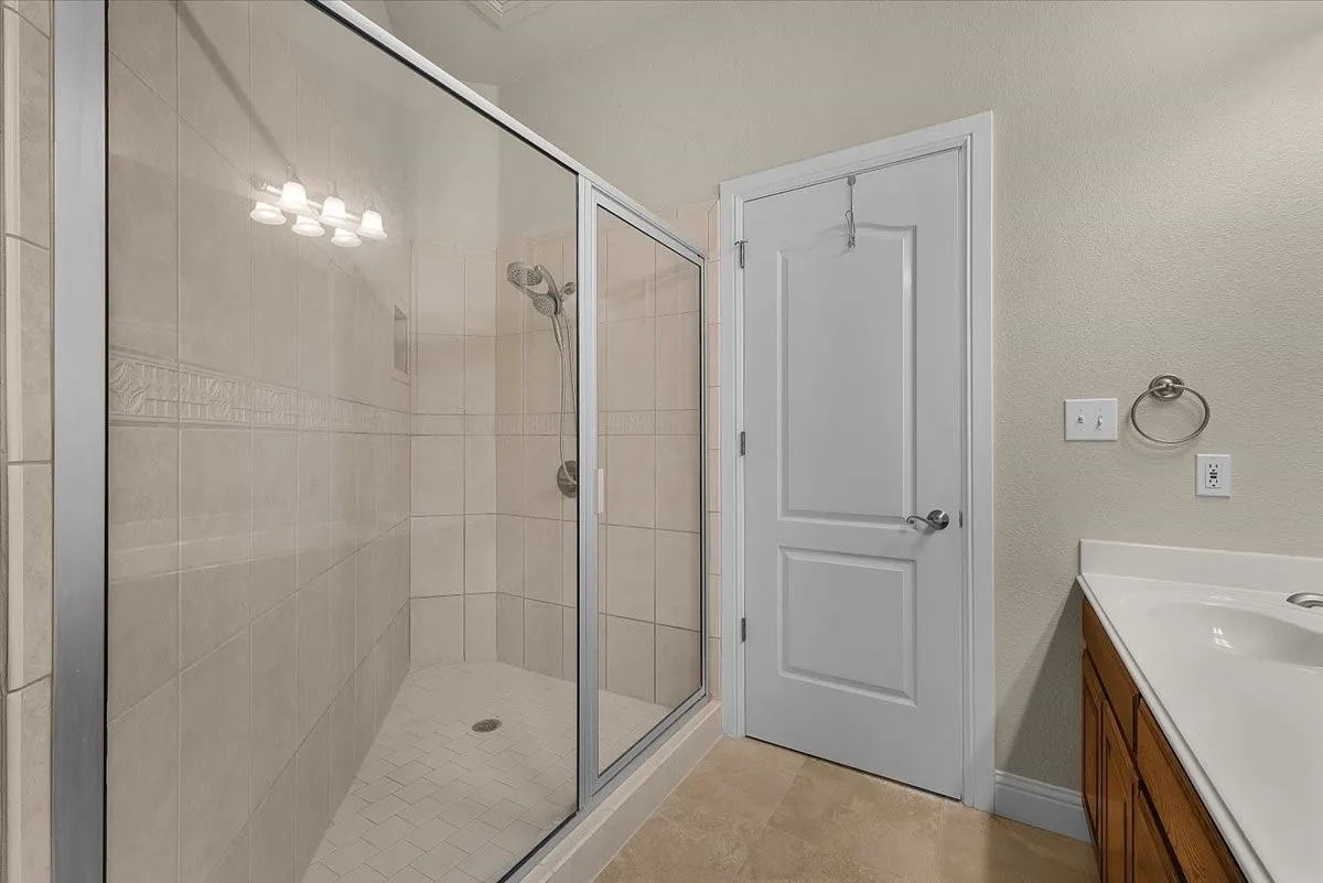 Tiled shower enclosure with glass surround, light-toned wall tiling, decorative accent band, and a brushed nickel shower head