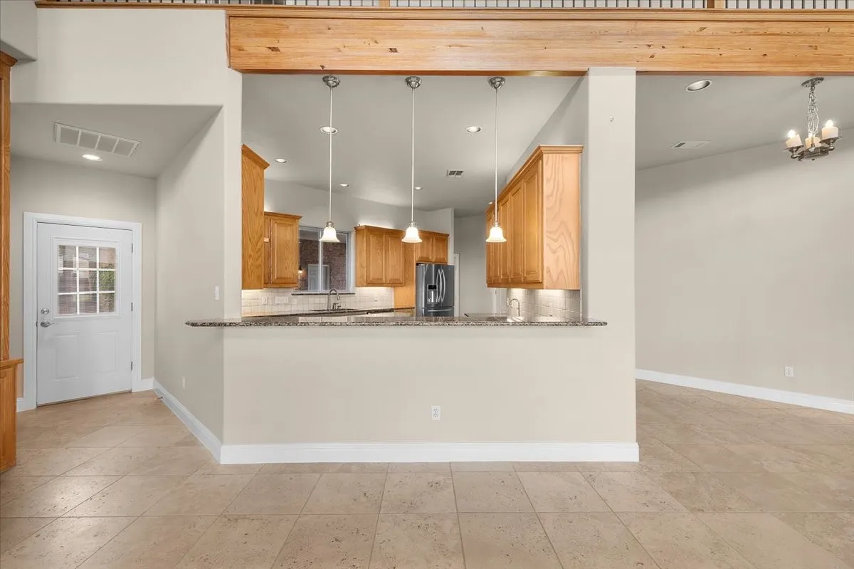 Open concept kitchen featuring warm wood cabinetry, granite countertops, and three pendant lights over a breakfast bar