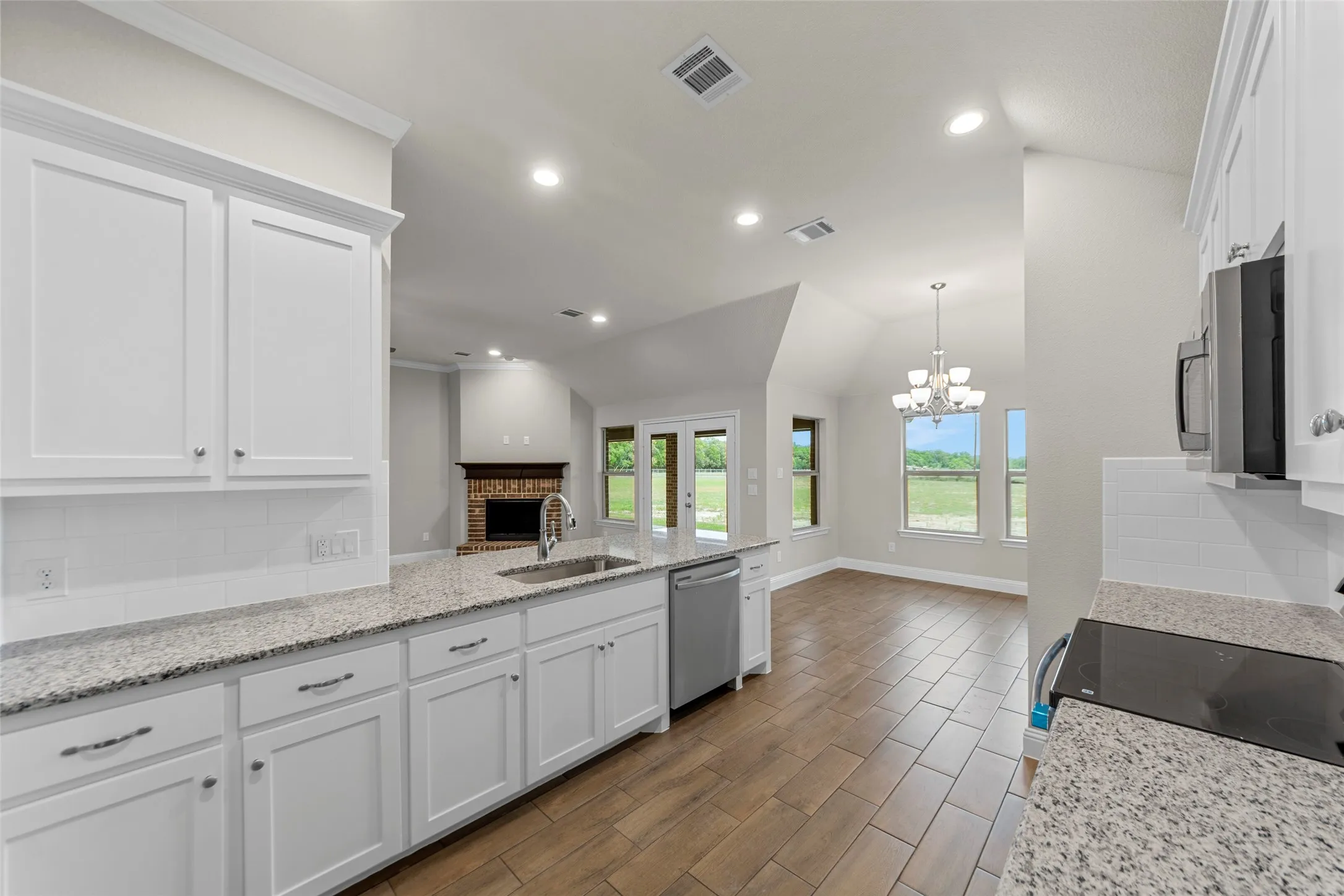 Kitchen featuring white cabinetry, light-toned granite countertops, a stainless steel sink with a gooseneck faucet, and wood-finish flooring