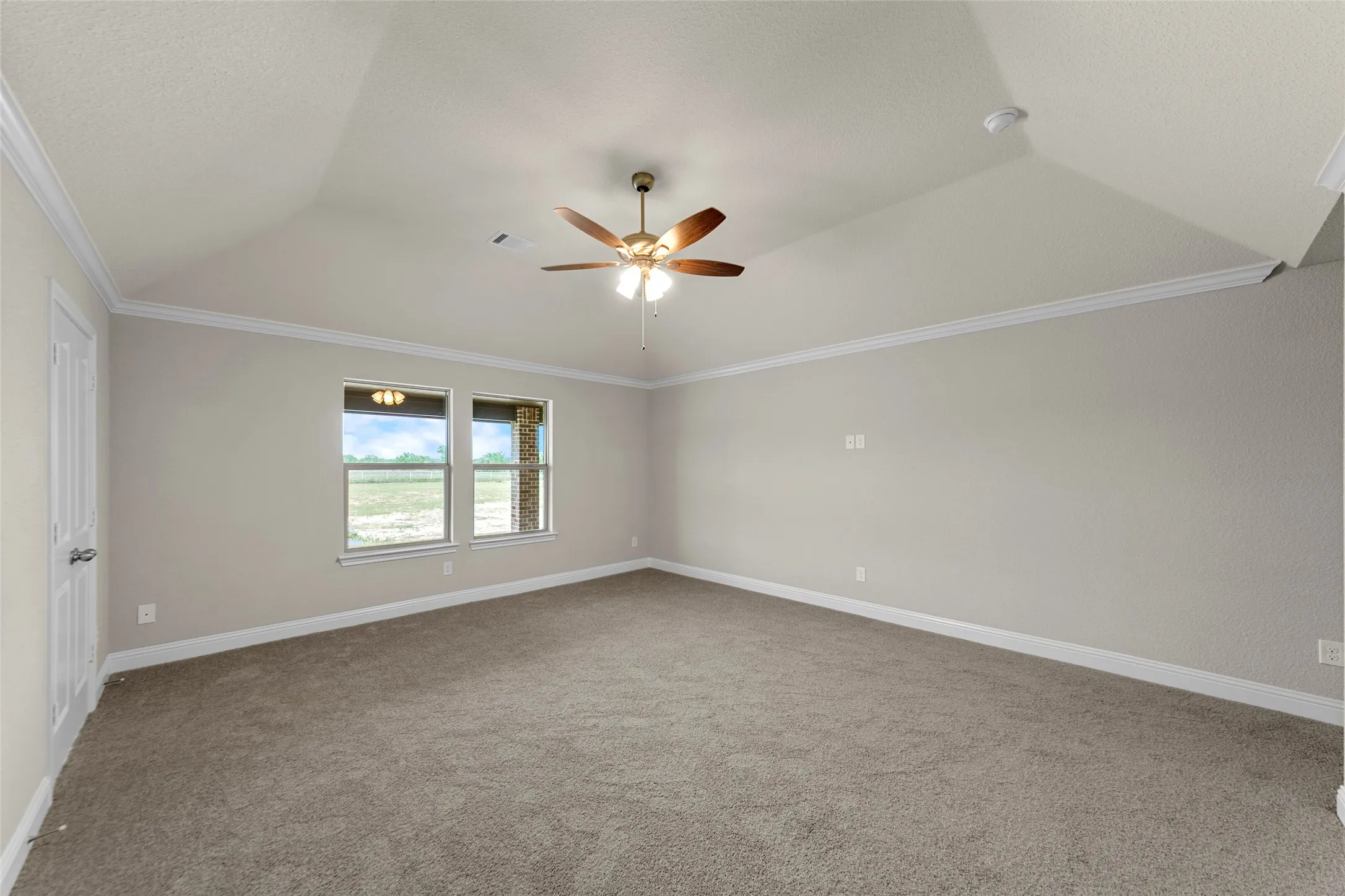 Spacious room featuring vaulted ceilings, crown molding, a ceiling fan, and carpeted flooring