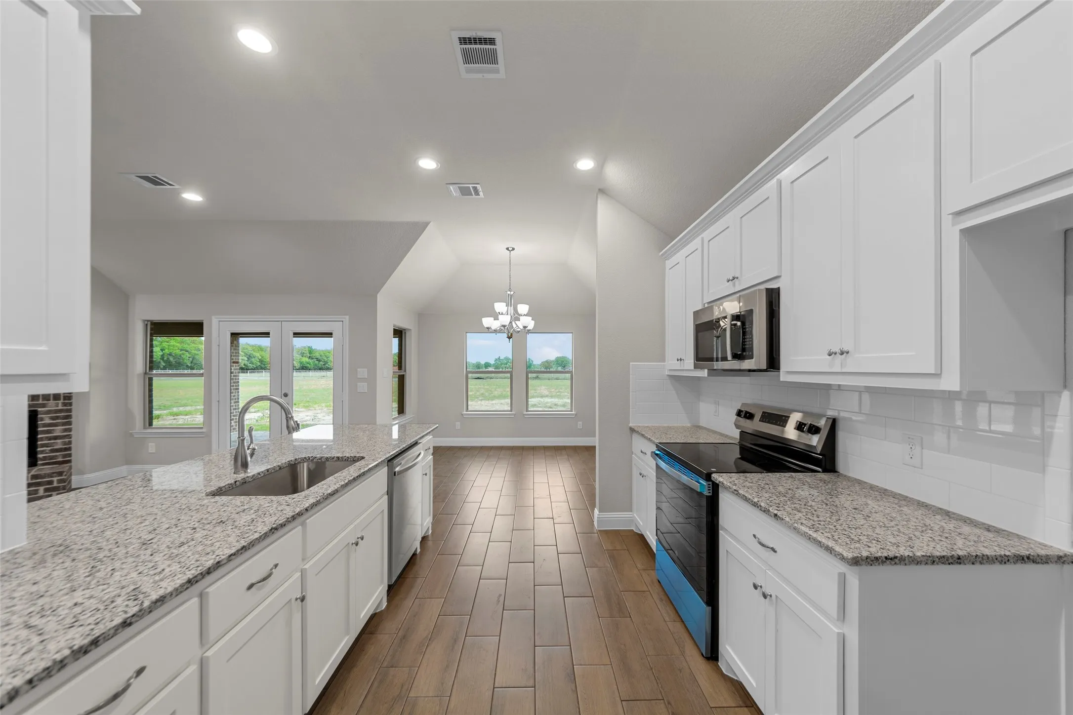 Kitchen featuring a deep stainless steel sink, granite-style countertops, wood-finish flooring, white cabinetry, and stainless steel appliances