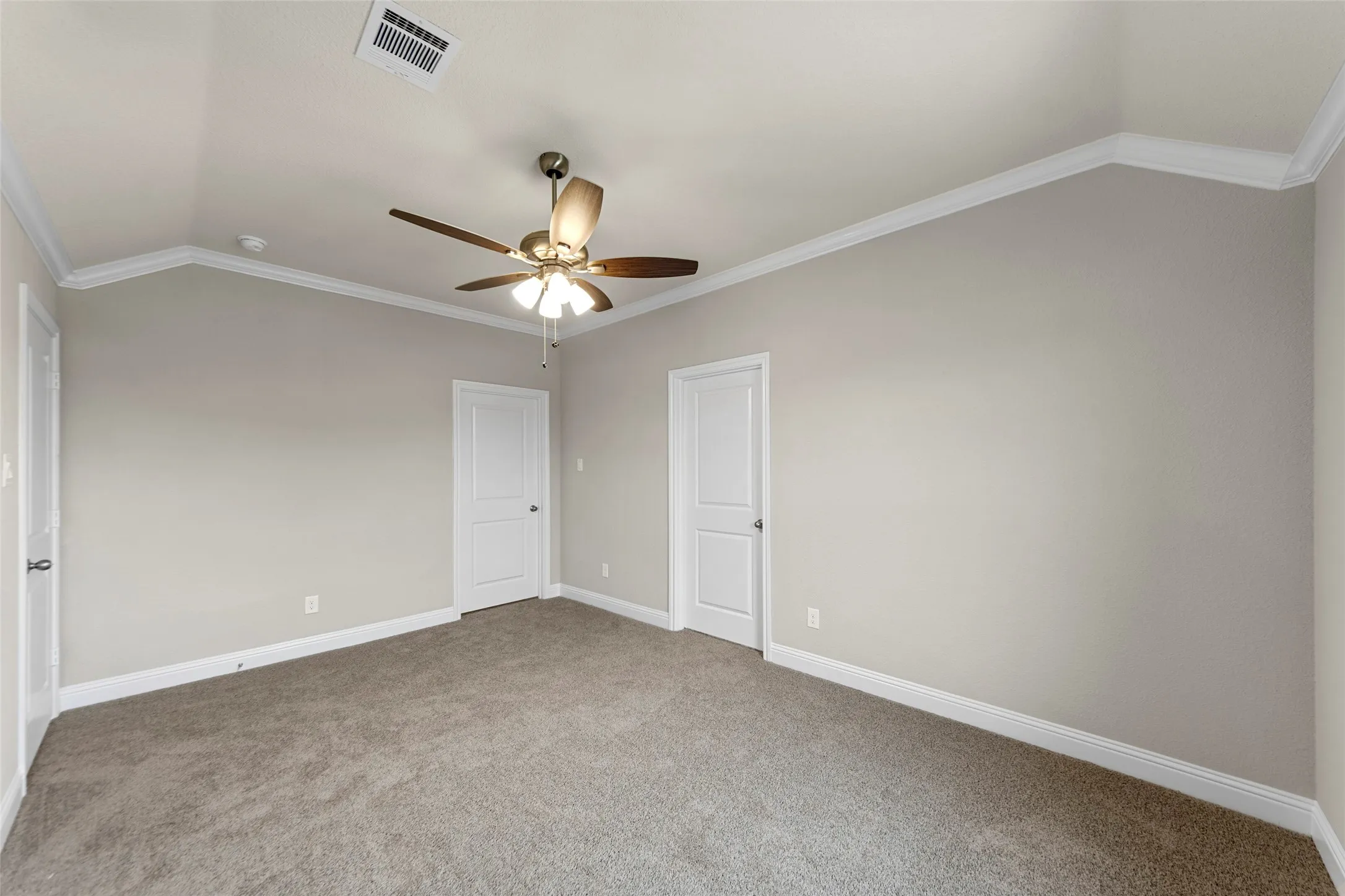 Carpeted room featuring a vaulted ceiling with crown molding, two panel doors, a ceiling fan with light kit, and neutral wall paint