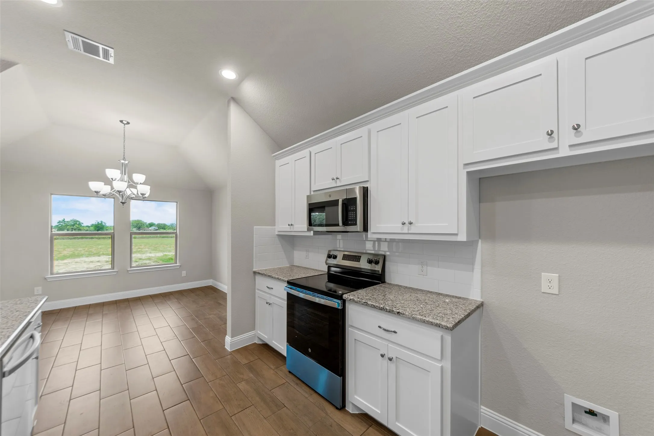 Kitchen and dining area featuring white cabinetry, stainless steel appliances, granite countertops, and a white subway tile backsplash