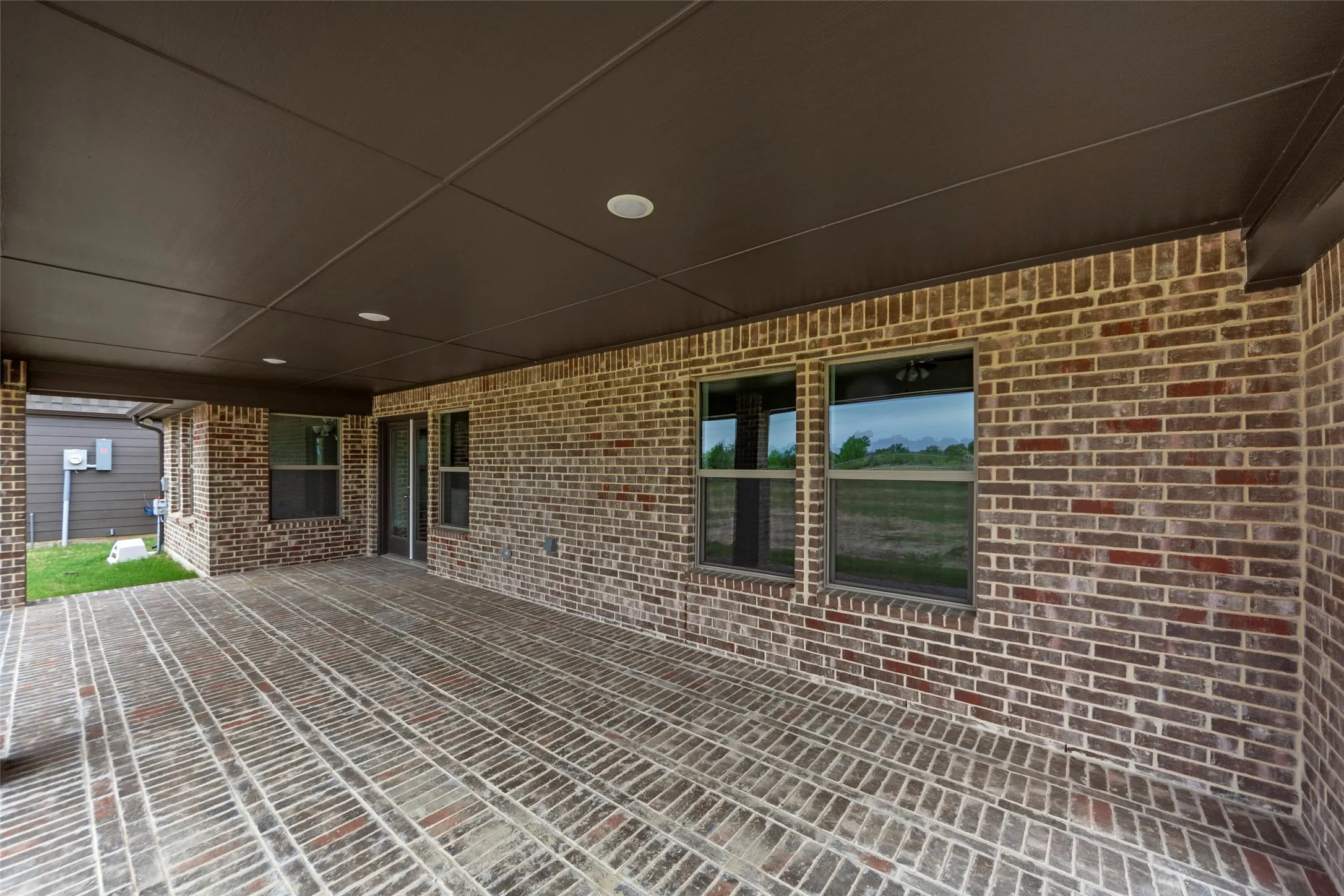 Covered outdoor patio featuring brick flooring, recessed lighting, and a dark ceiling