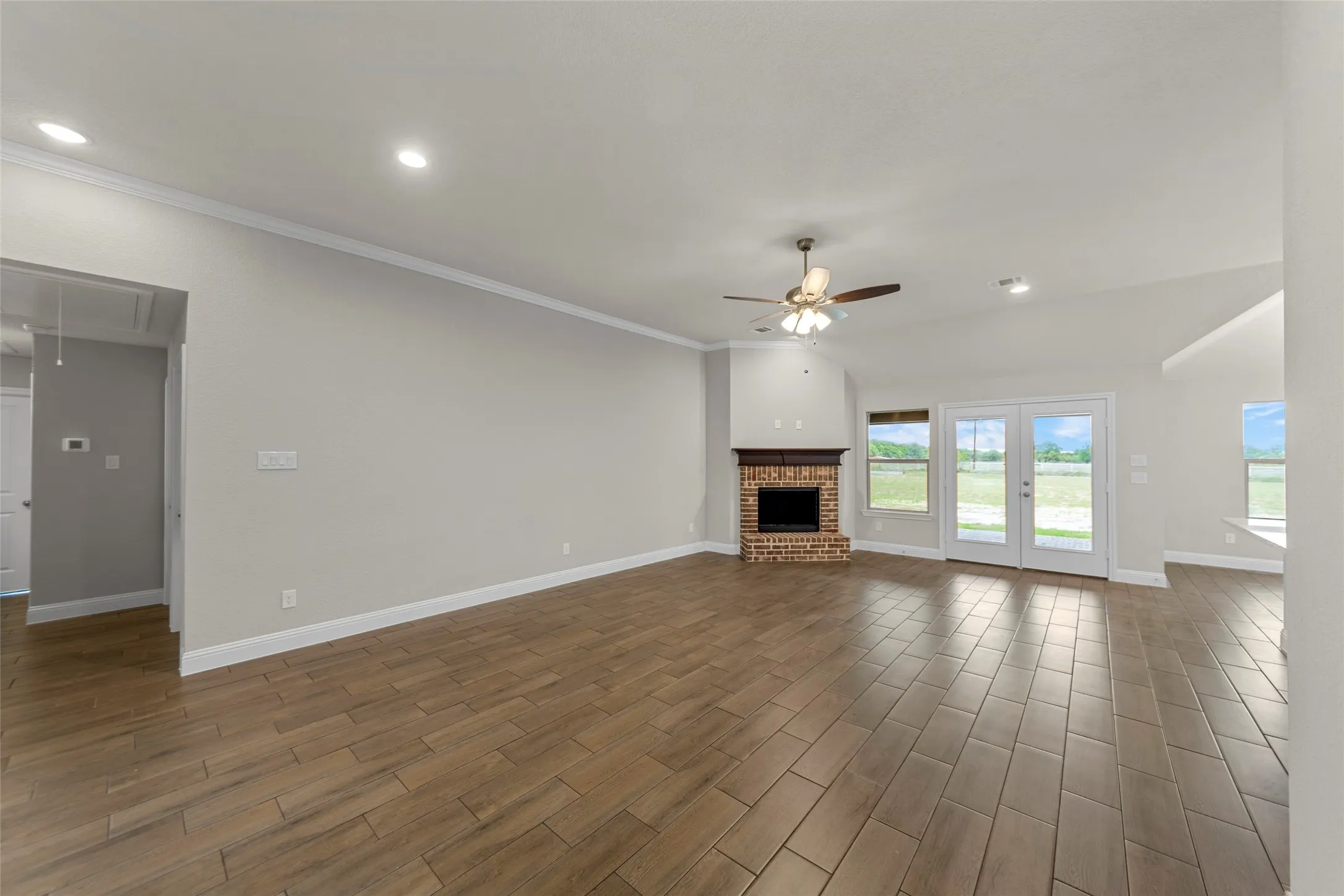 Spacious living area featuring wood-finish tile flooring, a brick fireplace with a wood mantle, and French doors