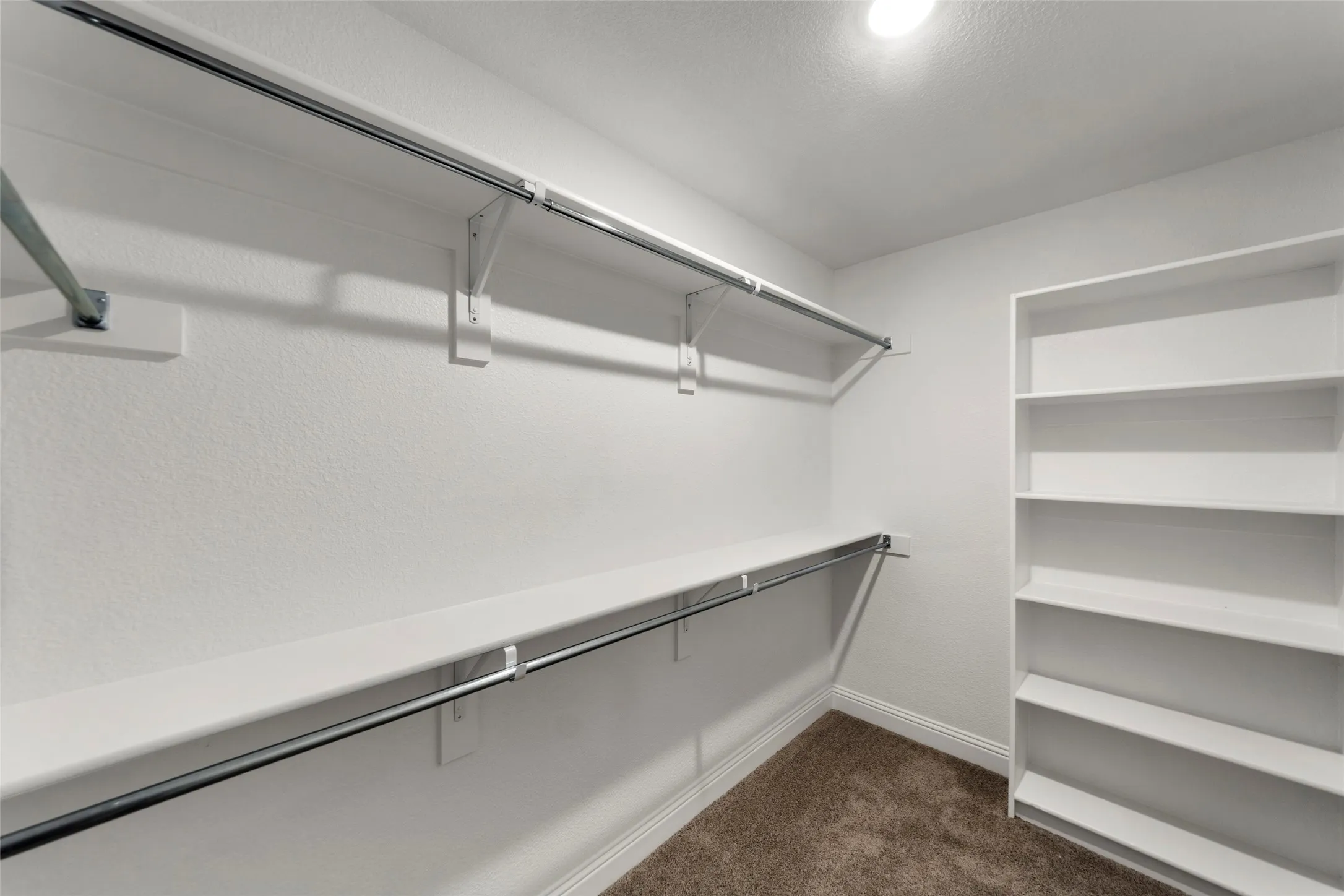 Walk-in closet featuring white walls, chrome hanging rods, and built-in shelving