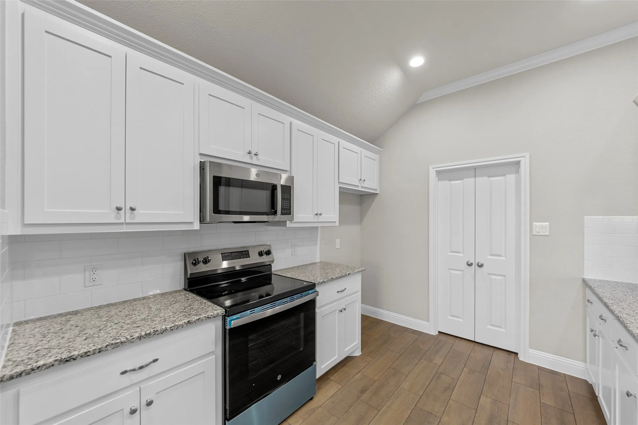 Kitchen featuring white shaker cabinetry, stainless steel appliances, speckled stone countertops, and a subway tile backsplash