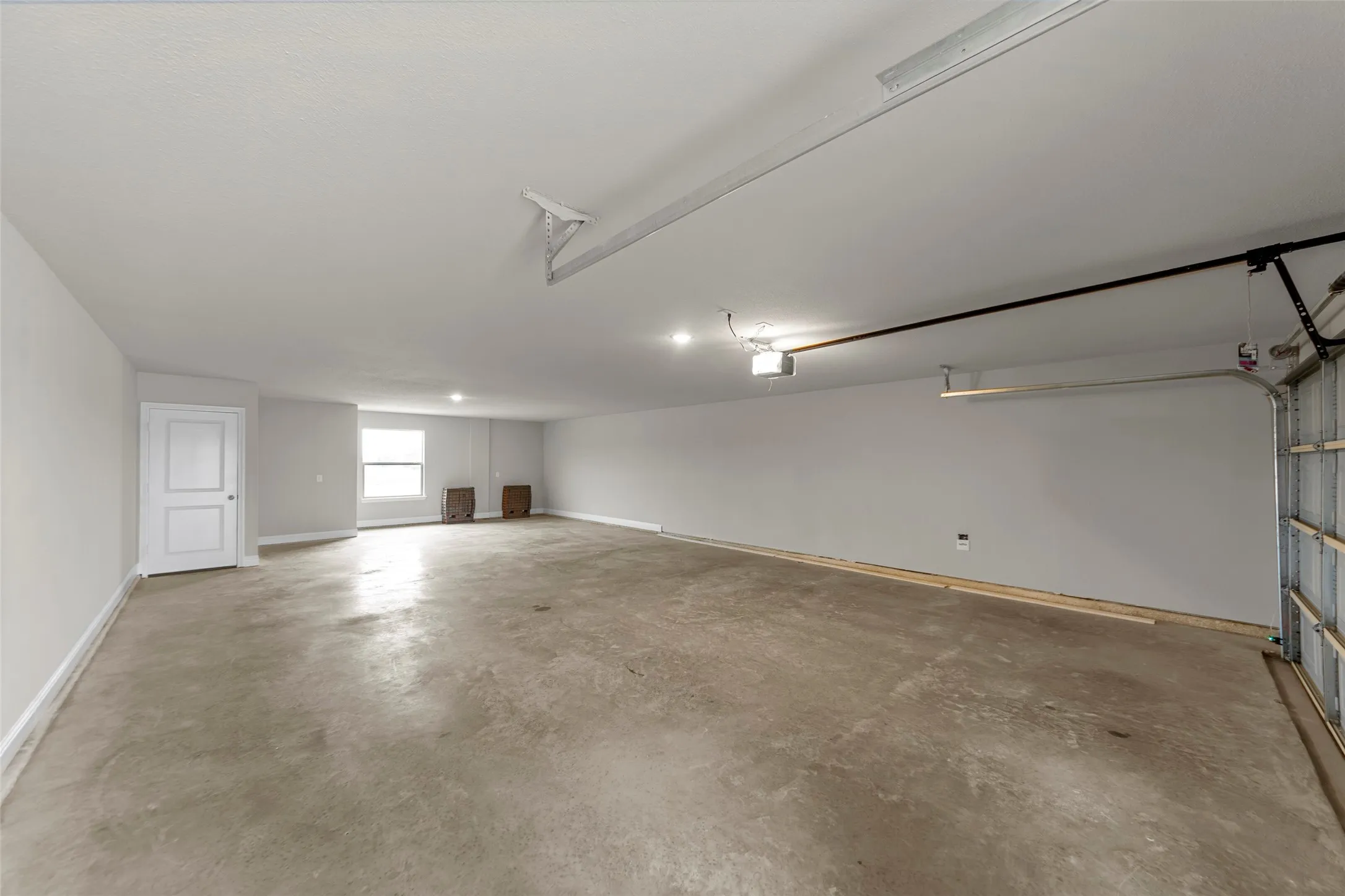 Spacious garage featuring a concrete floor, bright overhead lighting, and a white interior door