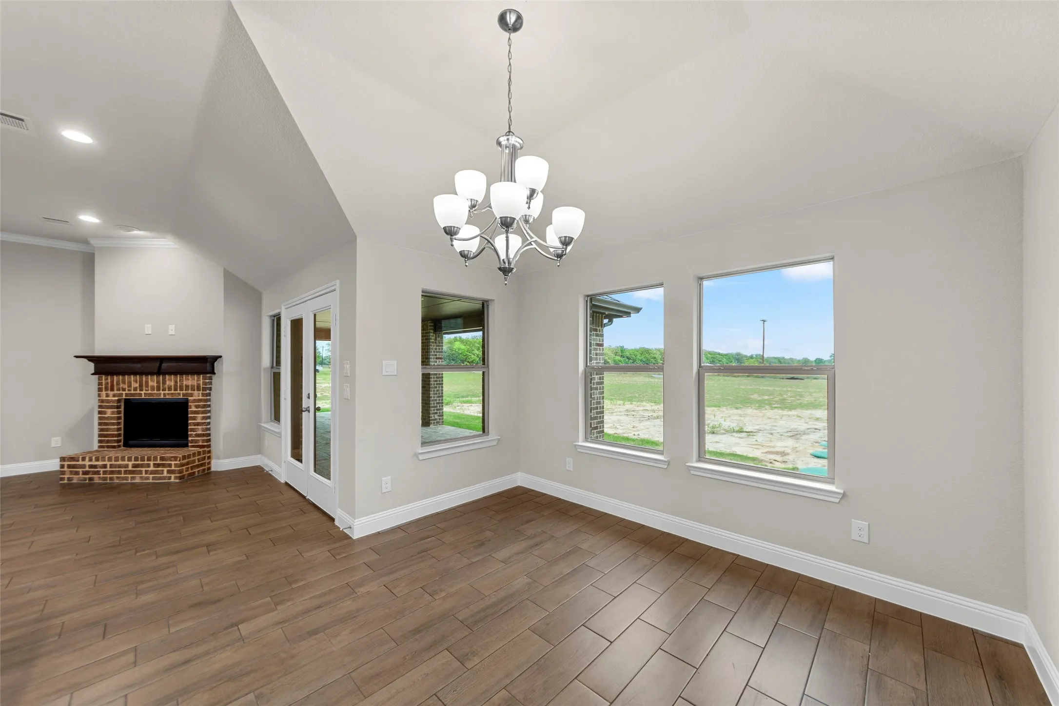Open concept living space featuring vaulted ceilings, wood-finish flooring, a brick-surround fireplace with a wood mantle, and a glass-paneled door
