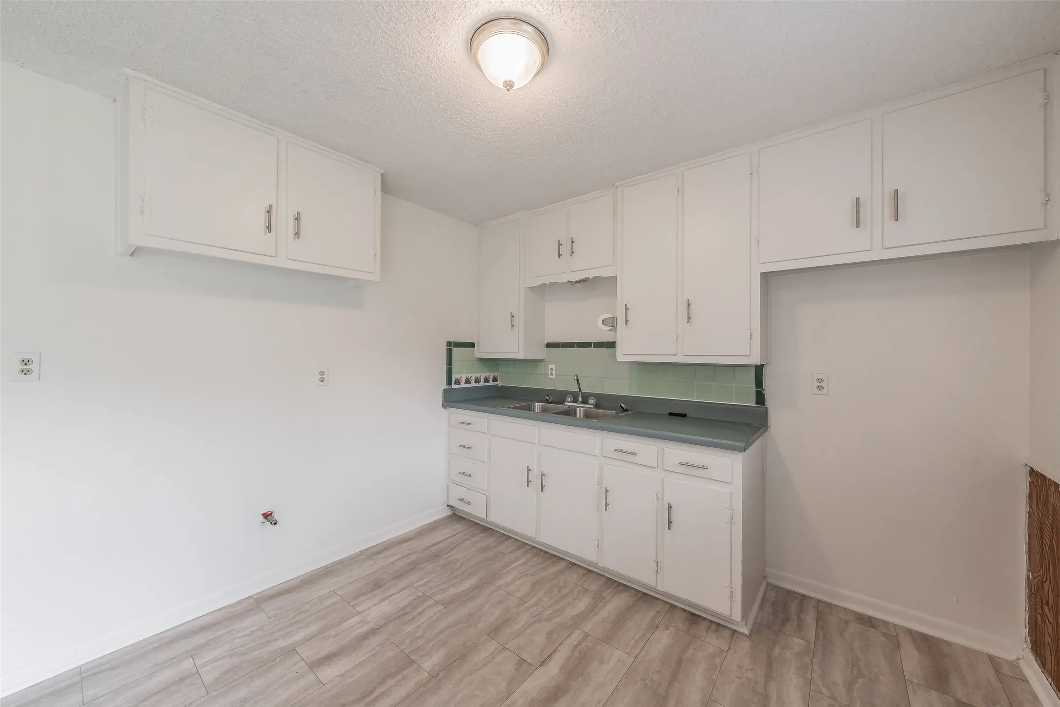 Kitchen featuring white cabinetry, light wood-finish flooring, a light green countertop, and matching green subway tile backsplash