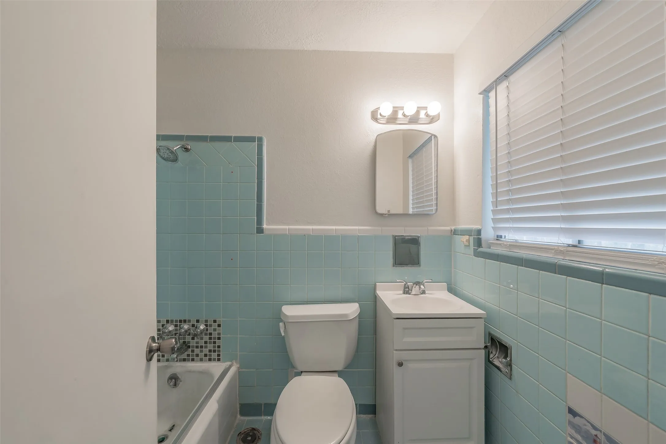 Bathroom featuring full tile walls, a built-in bathtub with shower, and a single-sink vanity