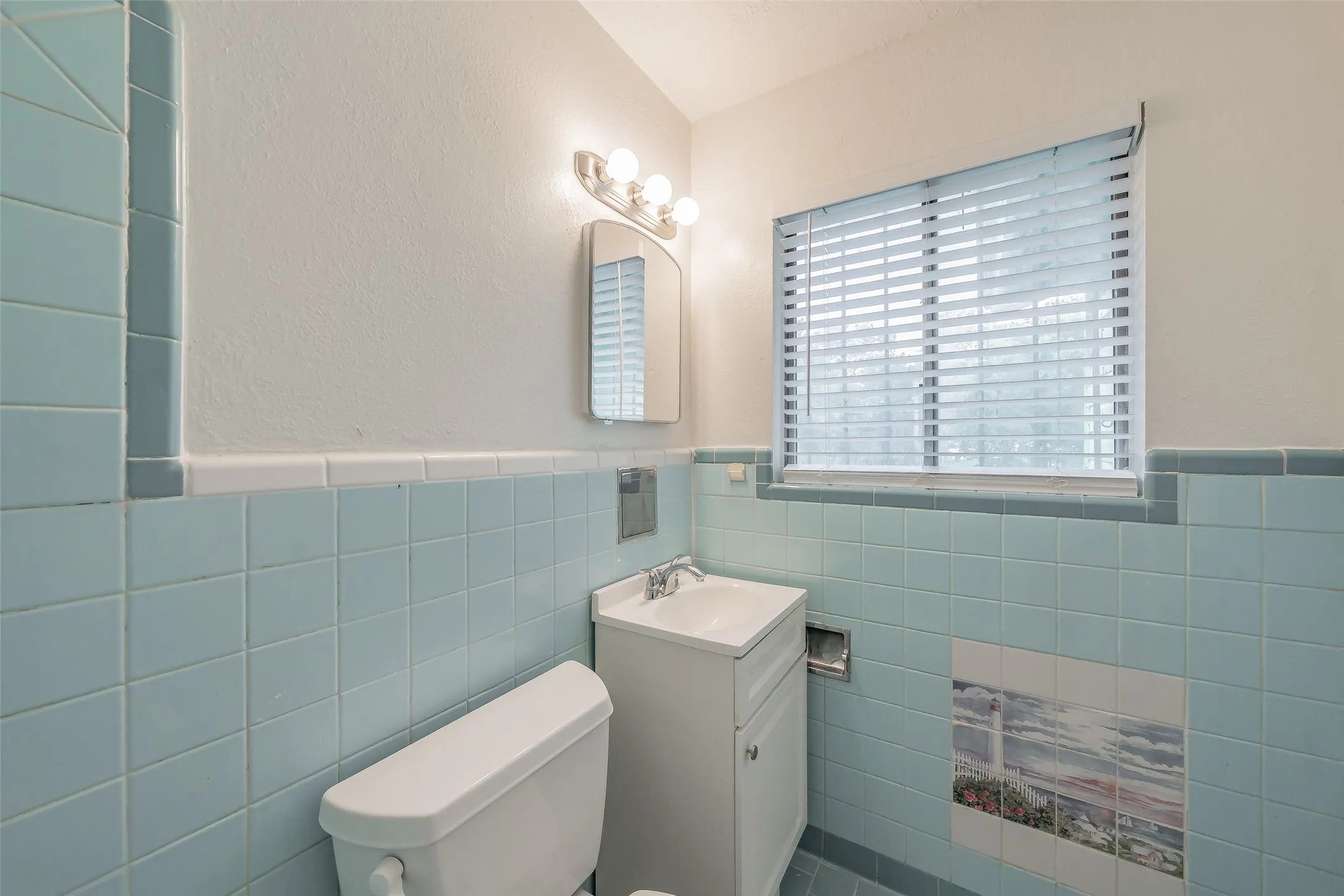 Bathroom featuring blue wall tiling, white vanity with sink, mirror, and window with horizontal blinds