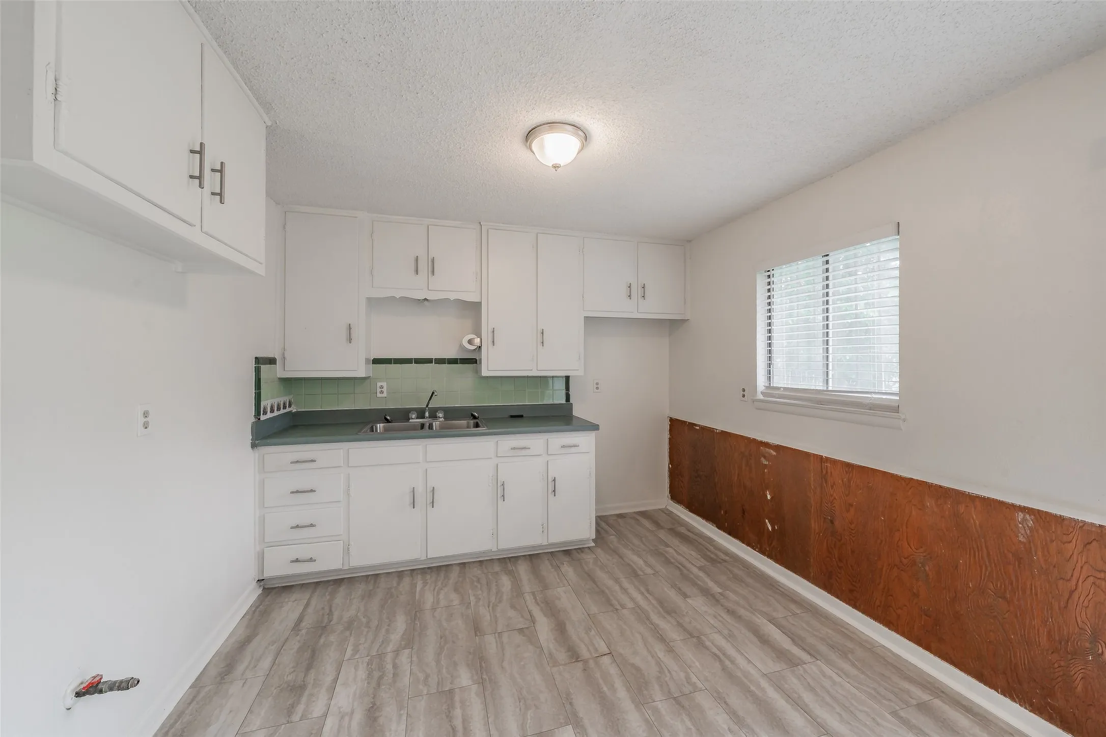 Kitchen area featuring white cabinetry, a double basin sink, green tile backsplash, laminate countertops, and wood-finish flooring