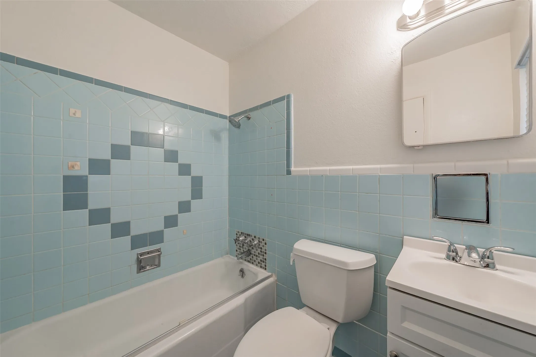 Bathroom featuring a full bathtub with shower, light blue wall tiles, and an integrated vanity with a white basin