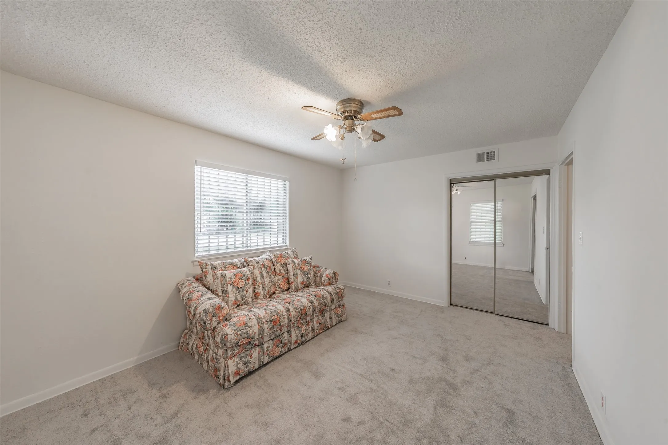 Carpeted room featuring a window with horizontal blinds, a ceiling fan with light fixture, and mirrored closet doors