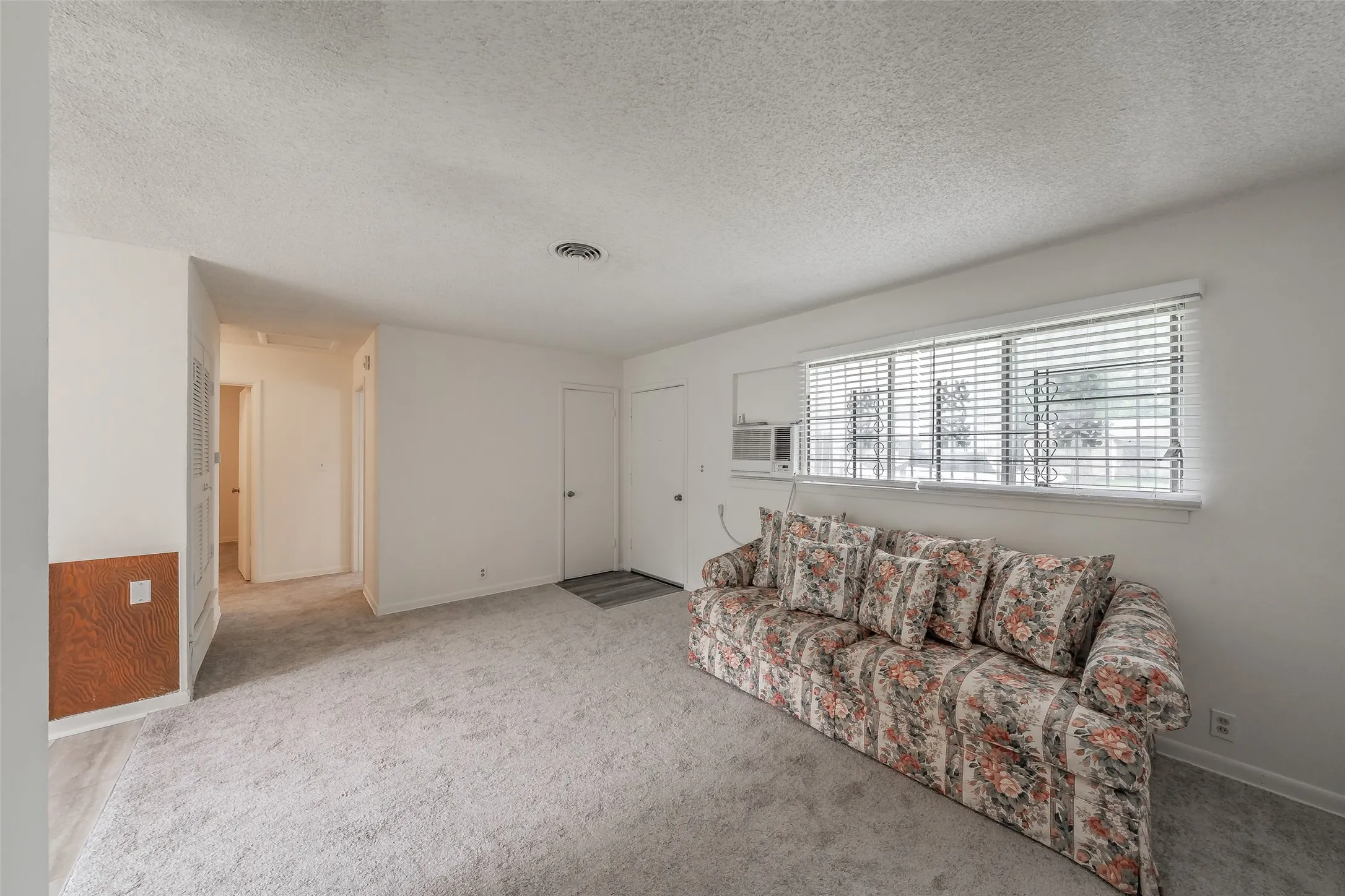 Carpeted interior space featuring a window with horizontal blinds, a ceiling-mounted air vent, and a hallway entrance