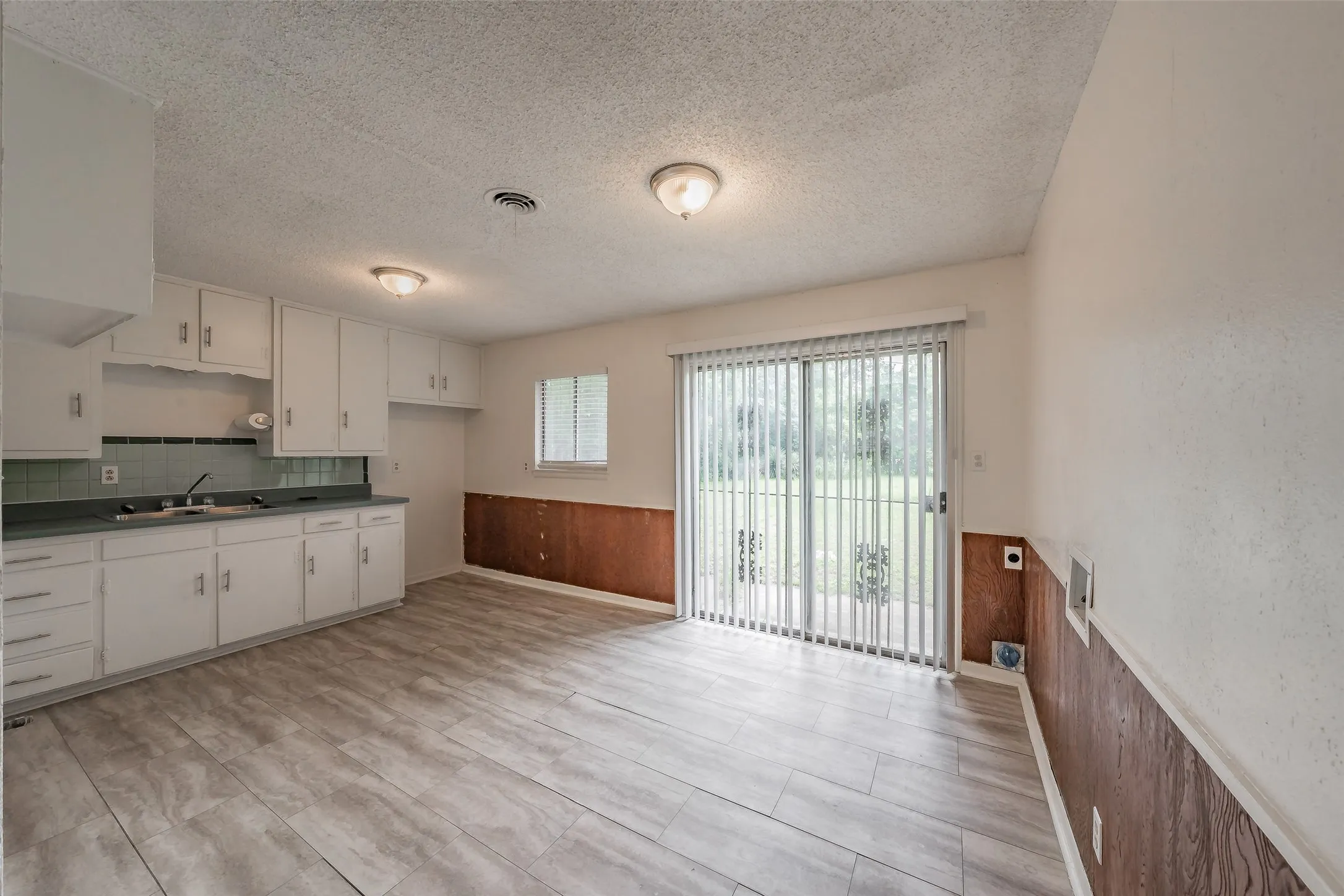 Kitchen and dining area featuring light wood-finish flooring, white cabinetry, and a teal tile backsplash