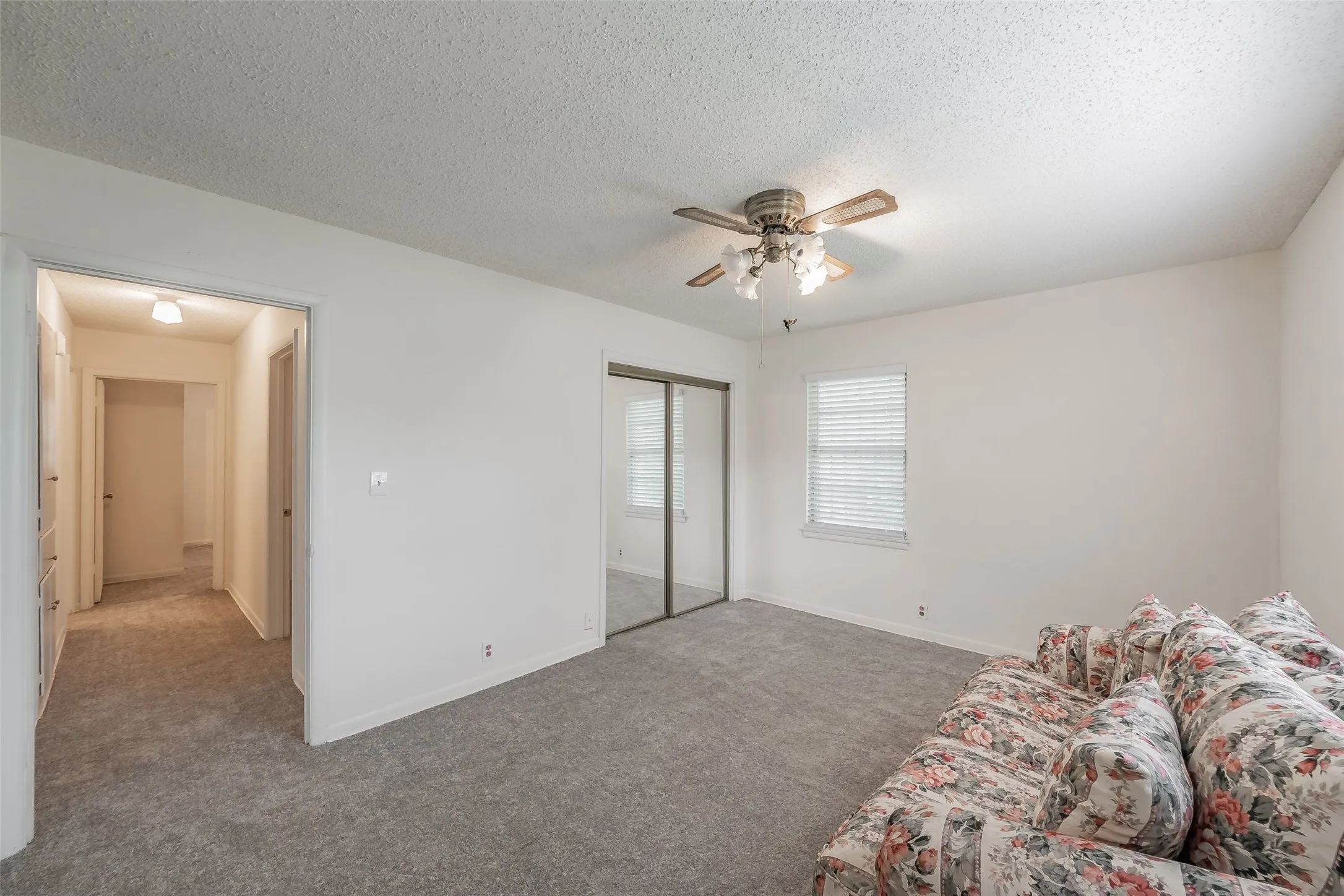 Bedroom featuring neutral-toned carpeting, a ceiling fan with light fixture, mirrored closet doors, and a window with blinds