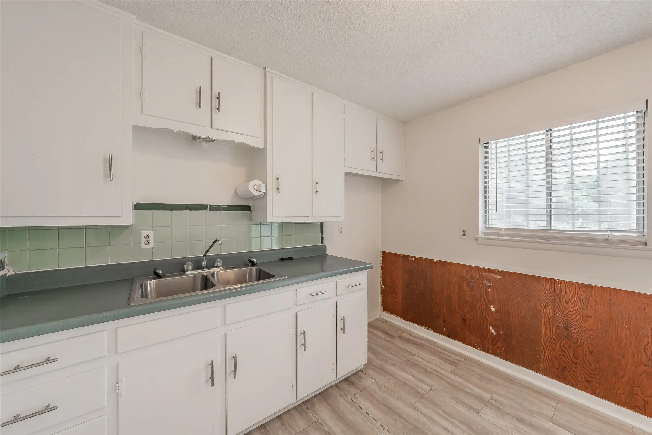 Kitchen featuring white cabinetry, a double basin stainless steel sink, light green tile backsplash, and light wood-finish flooring