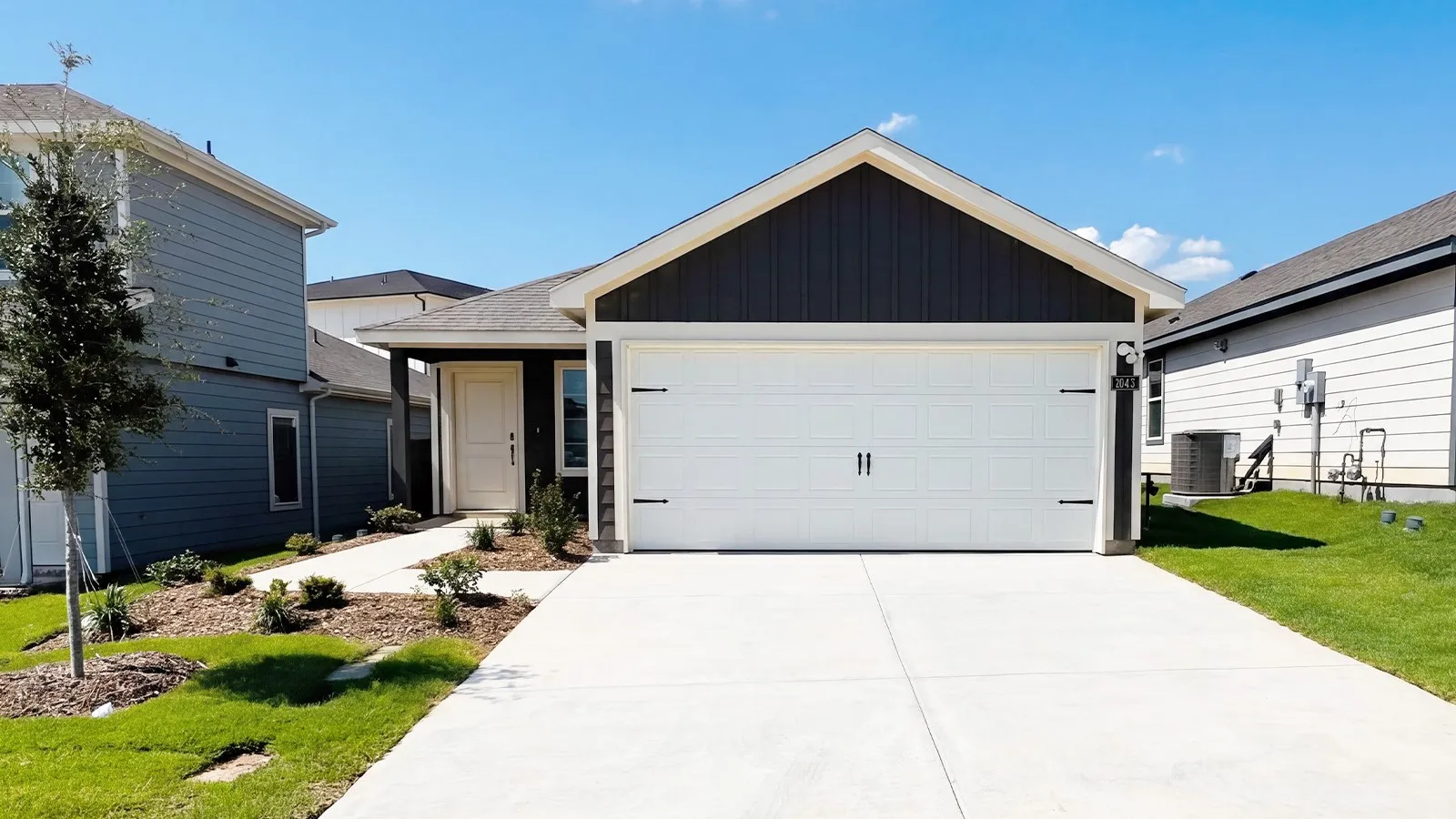 Contemporary exterior featuring a white garage door, dark siding, light-colored entry door, and a concrete driveway