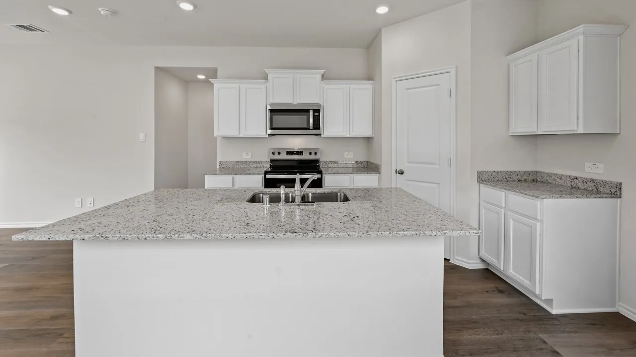 Spacious kitchen featuring a large island with an undermount sink, ample white cabinetry, stone countertops, and wood-finish flooring