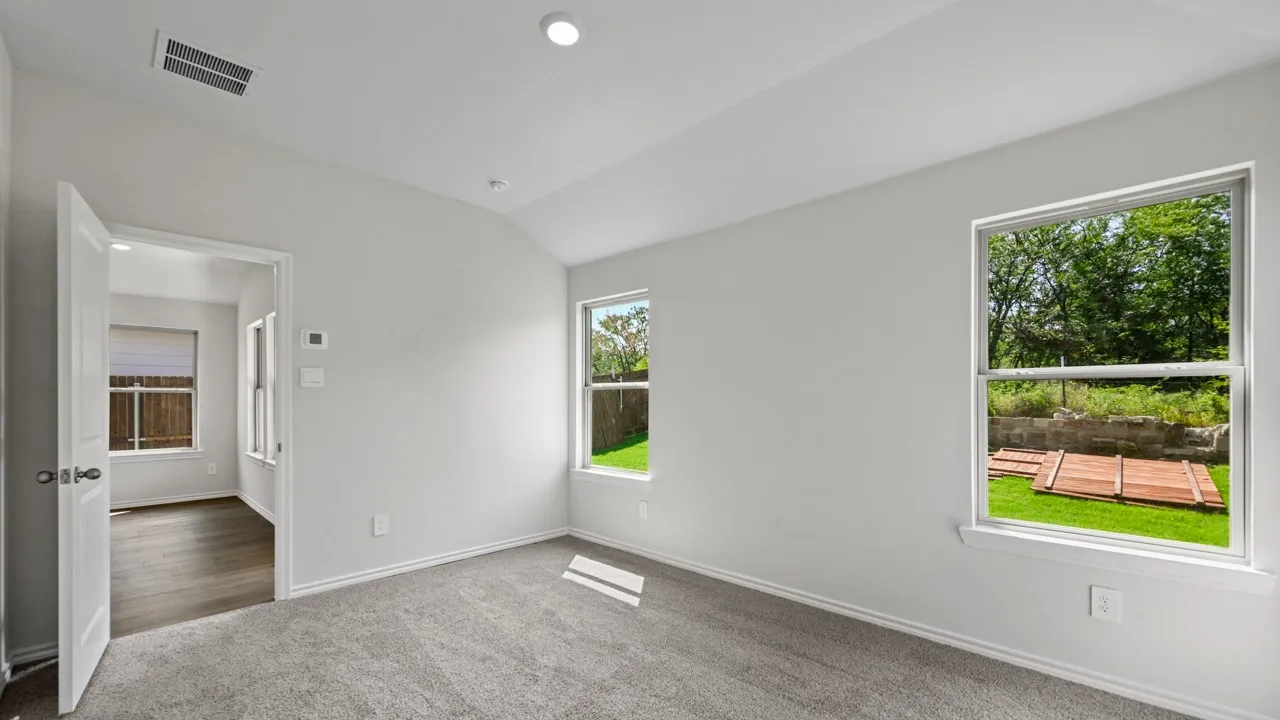 Carpeted room featuring two windows with outdoor views, light gray walls, and an open doorway leading to a room with wood-finish flooring