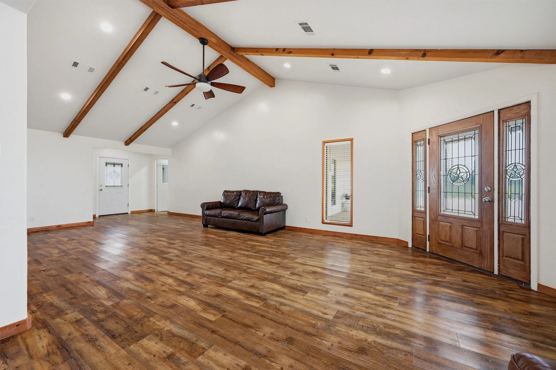 Residence living area has beamed ceilings, ceiling  fan and  cut glass entry door with sidelights