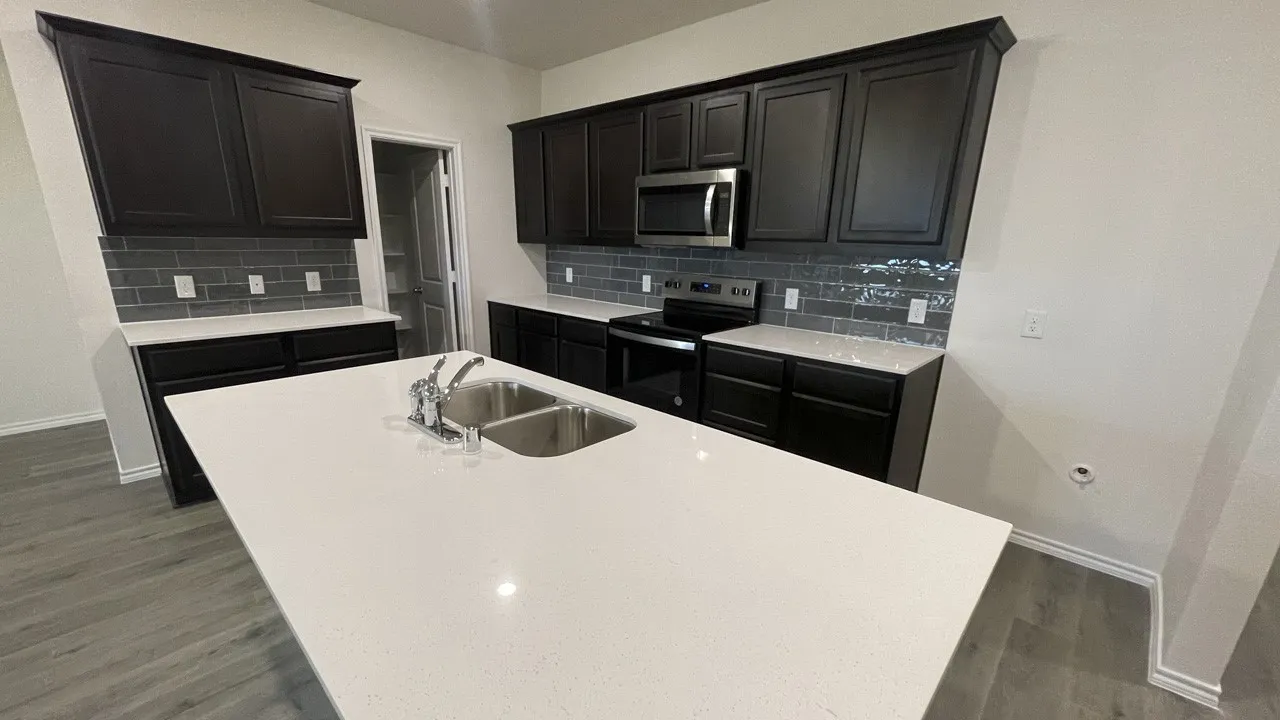 Spacious kitchen island with a double basin stainless steel sink, complemented by dark cabinetry, light countertops, and a gray subway tile backsplash