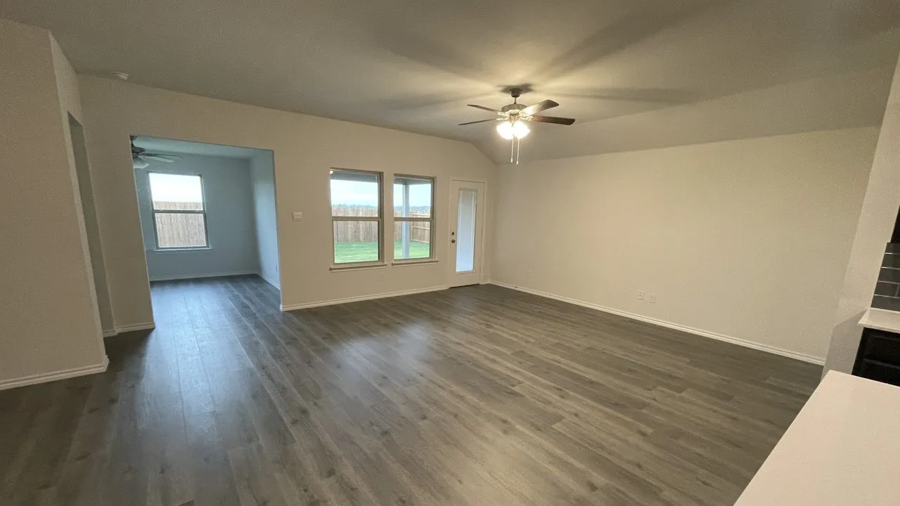 Spacious interior featuring wood-finish flooring, ample natural light from multiple windows, an open-concept layout, a ceiling fan with integrated lighting, and a glass-paneled exterior door