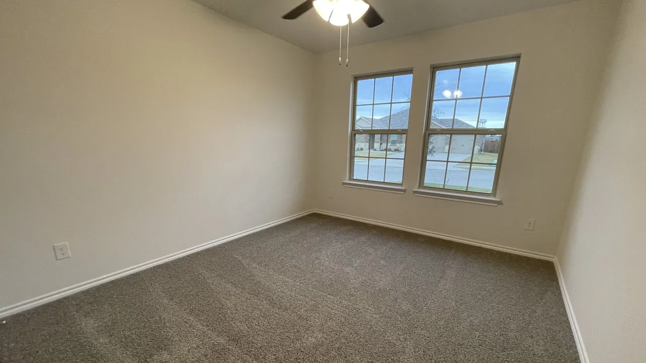 Bright room featuring two large windows with grid patterns, neutral-toned carpet flooring, and a ceiling fan with integrated lighting