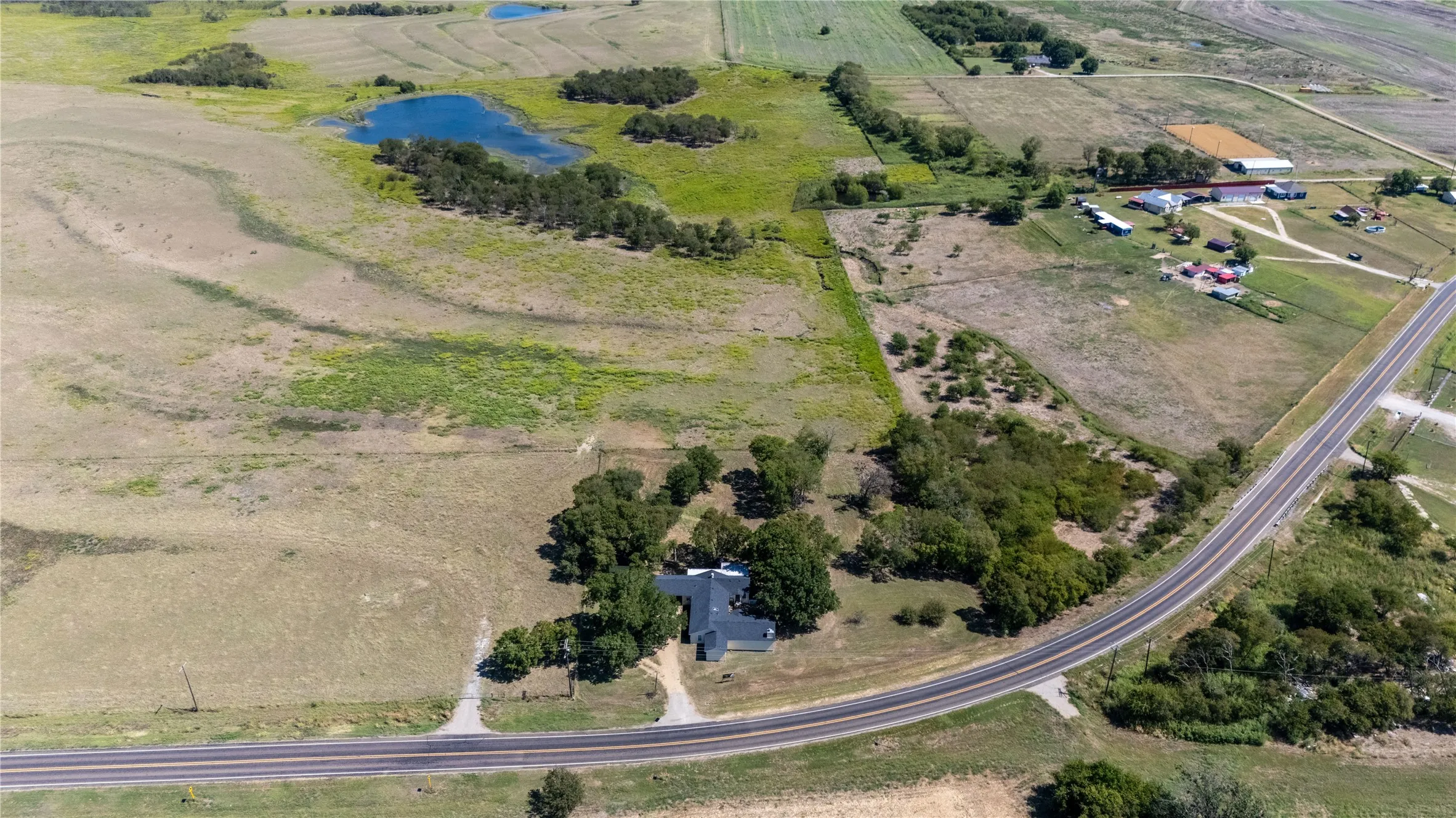 Aerial view of the property, featuring a residential structure with a gray roof and surrounding trees, situated alongside a paved road
