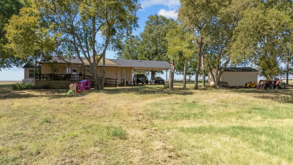 The property features an extensive yard with mature trees, a covered porch, and a dedicated carport
