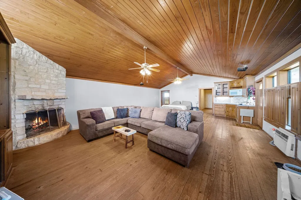 Spacious living area featuring a stone fireplace, wood floors, and a vaulted wood-paneled ceiling with ceiling fans