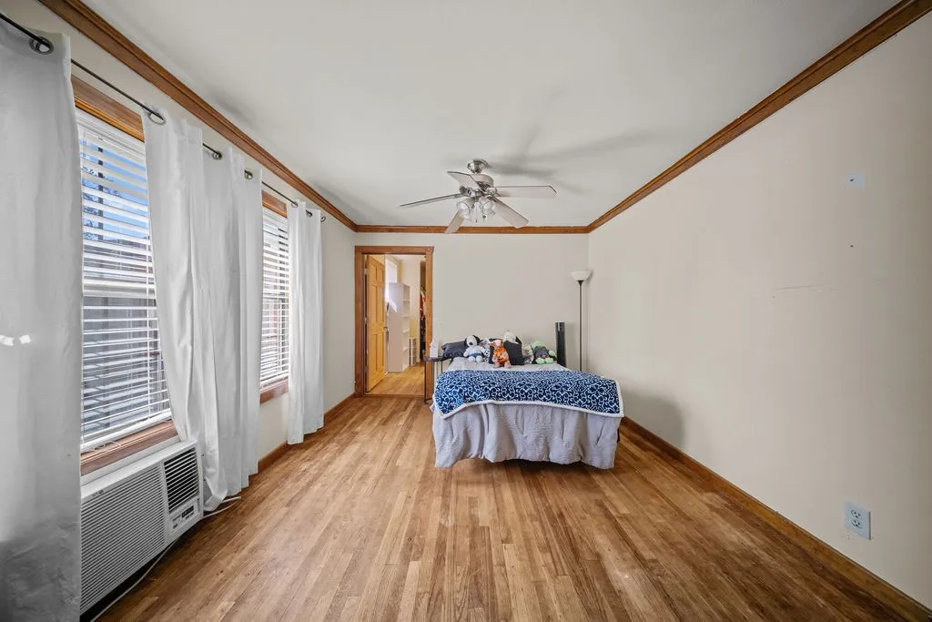 Spacious room featuring hardwood flooring, multiple windows providing natural light, and a ceiling fan