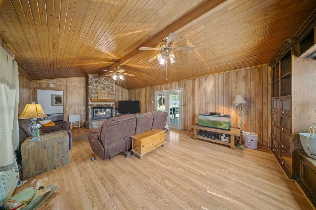 Living area featuring natural wood paneling on walls and ceiling, hardwood floors, a stone fireplace, and French doors