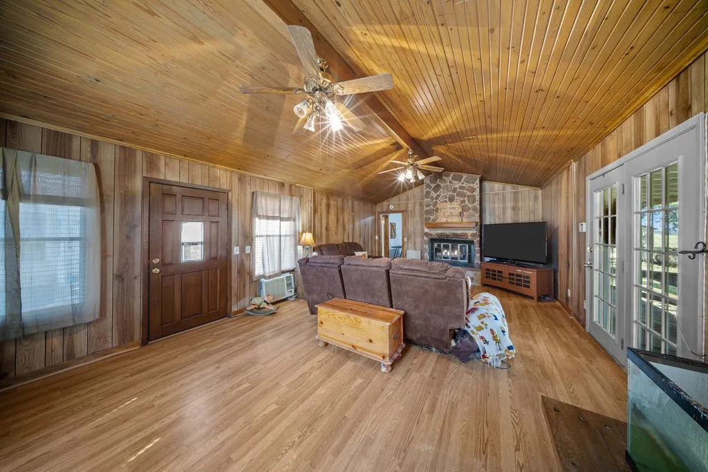 The living area features wood paneling on the walls and ceiling, hardwood flooring, and a stone fireplace