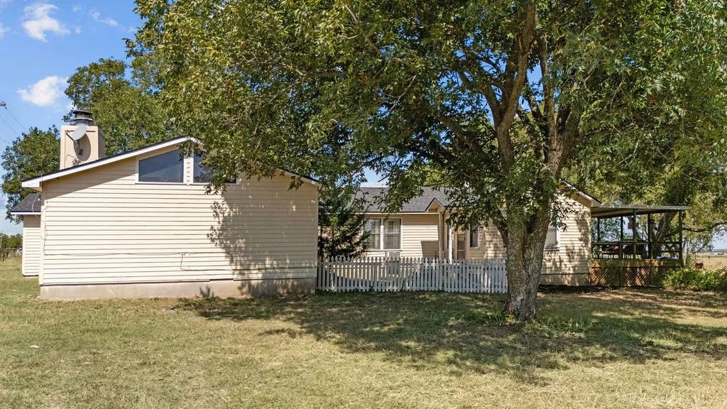The property features a well-maintained lawn and mature trees, with a white picket fence enclosing a section of the yard