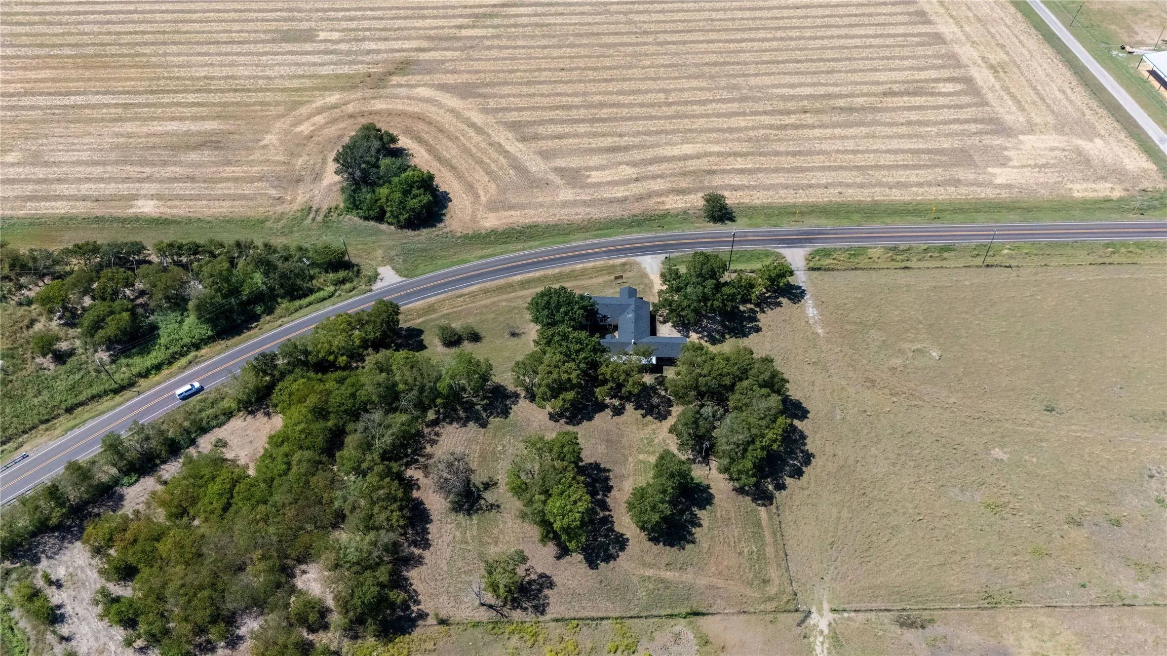The property features a residence surrounded by mature trees, situated alongside a road