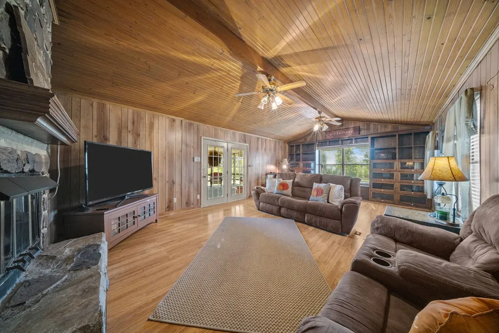 The inviting living space features wood paneling on the walls and vaulted ceiling, a substantial stone fireplace, and hardwood flooring