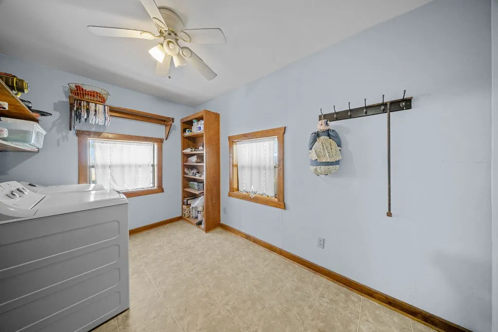 Utility room with light blue walls, two windows with wooden trim, and a ceiling fan